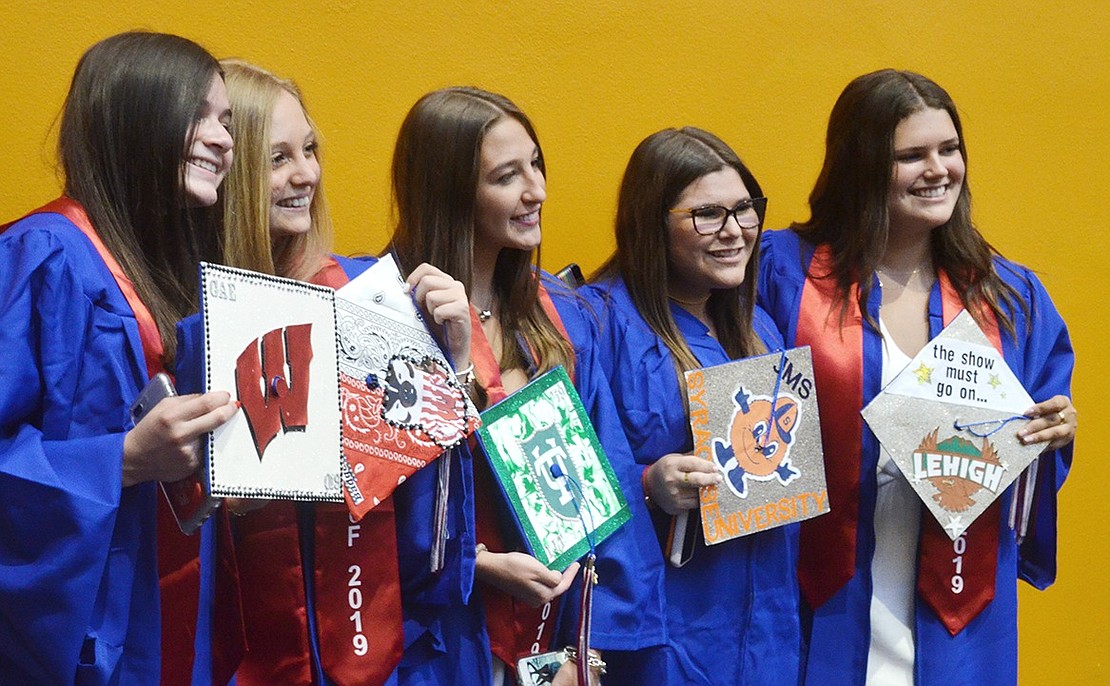 Gabby Egol (left), Allyson Jaffe, Lillianna Trevino, Jamie Solomons and Mackenzie Drangel hold up elaborately decorated graduation caps showing where they’ll be headed to college in the fall.