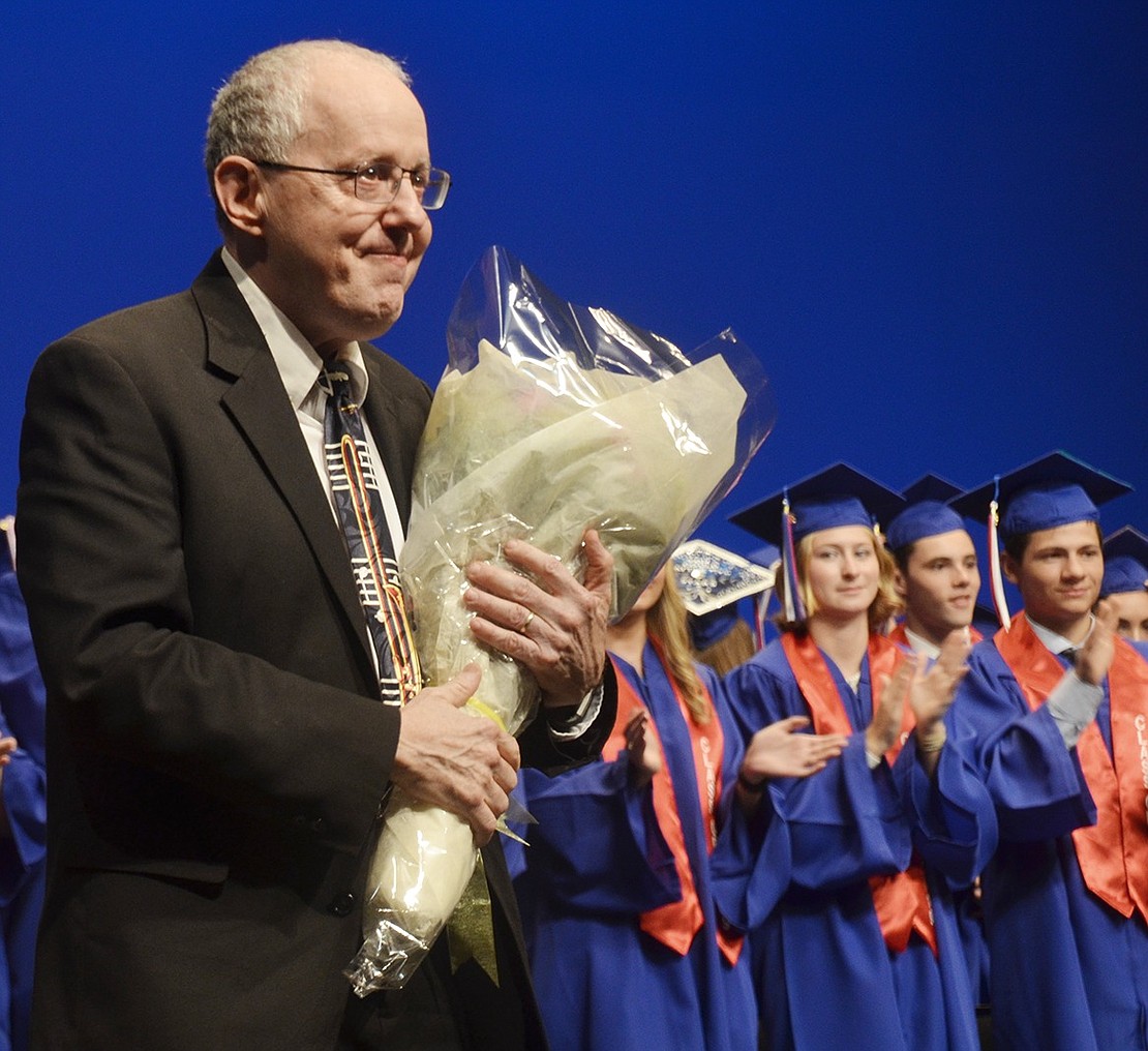 As the crowd applauds, retiring music teacher Howard Levy accepts a bouquet of flowers gifted to him by students honoring his last graduation ceremony.