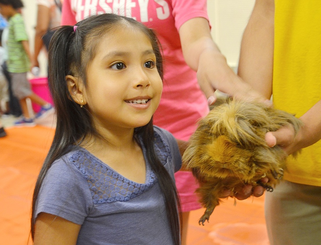 John F. Kennedy Elementary School rising second-grader Alexa Guncay smiles as she pets a long-haired guinea pig at the library.