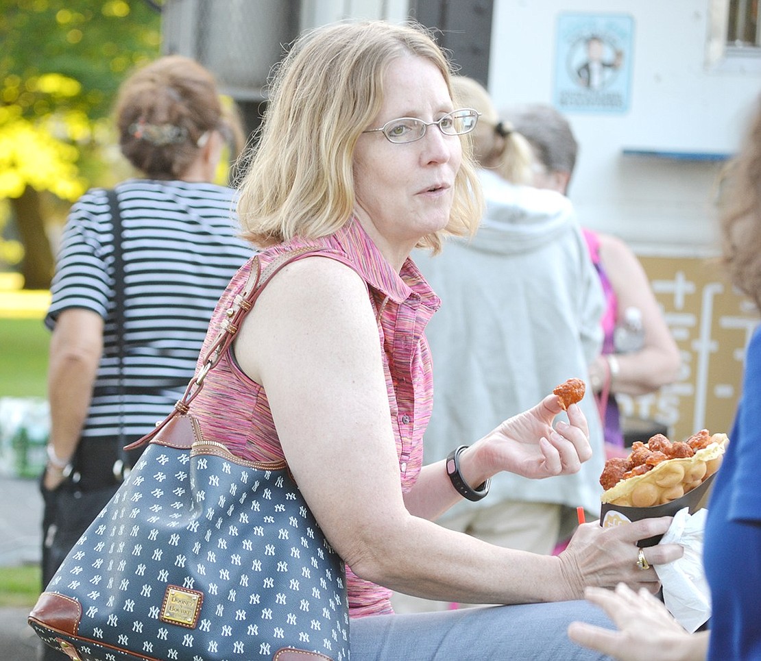 While waiting for the concert to start, Madison Avenue resident Christine Rosario chats with friends and snacks on her buffalo chicken waffle cone from the Waffle Box food truck. There will be various food truck vendors at every Friday night concert this summer.