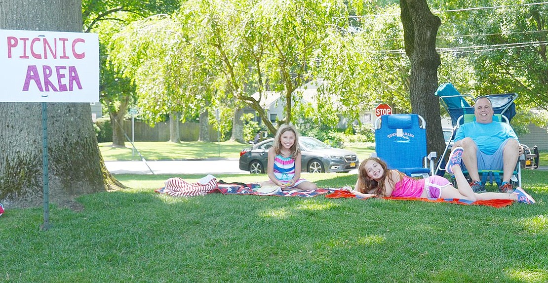 Taking a few minutes to beat the heat, Steven Stolzenberg (right) relaxes in his strategically shady picnic area with his daughter Jessica and her friend Ava Benoit, both rising fourth-graders at Ridge Street Elementary School. The Rye Brook residents are visiting Pine Ridge Park for lunch and classic games during the Village-sponsored old-fashioned picnic on Saturday, July 13.