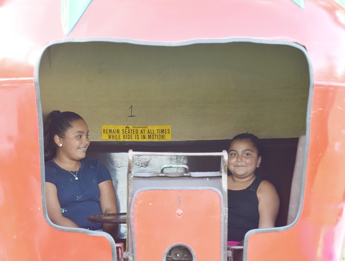 Enclosed in a giant metallic piece of fruit, Port Chester Middle School rising seventh-grader Lucelly Espinosa (left) and her 7-year-old sister Jayleen smile after spinning around on the Apple-Go-Round ride.