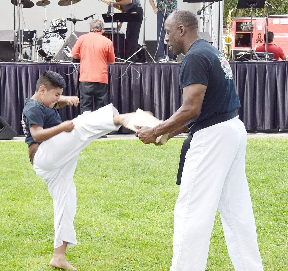 As Westchester World Tae Kwon Do Association instructor Russell Fulmore holds a wooden plank steady for a martial arts demonstration, 10-year-old Luis Diaz chops it into two pieces with his foot.