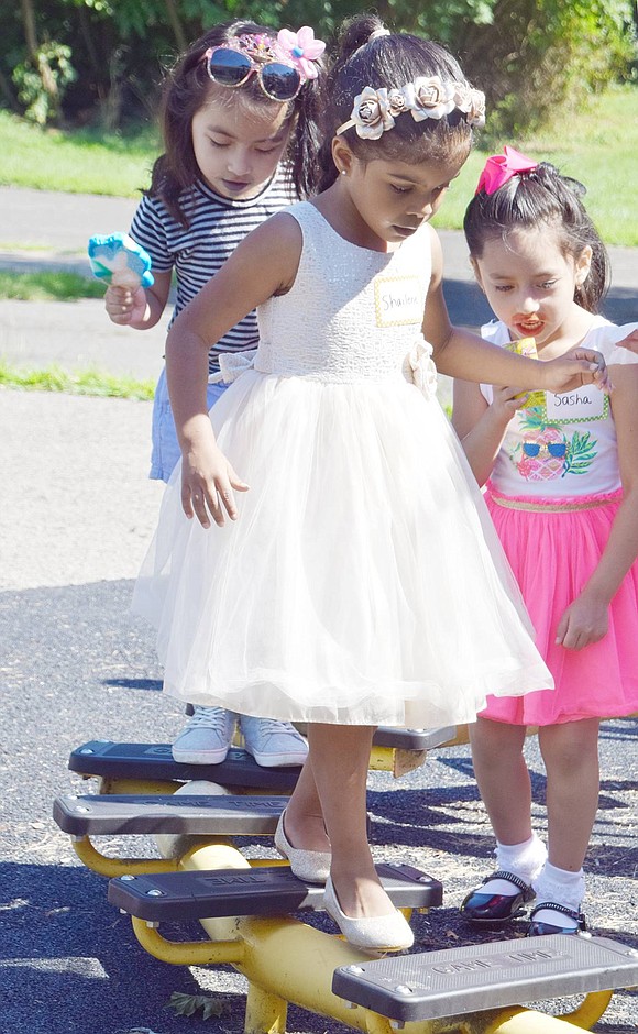 In her pretty white dress, Grandview Avenue resident Shailene Fernandez leads a group of other ice cream yielding John F. Kennedy School kindergarteners around a balancing obstacle on the playground.