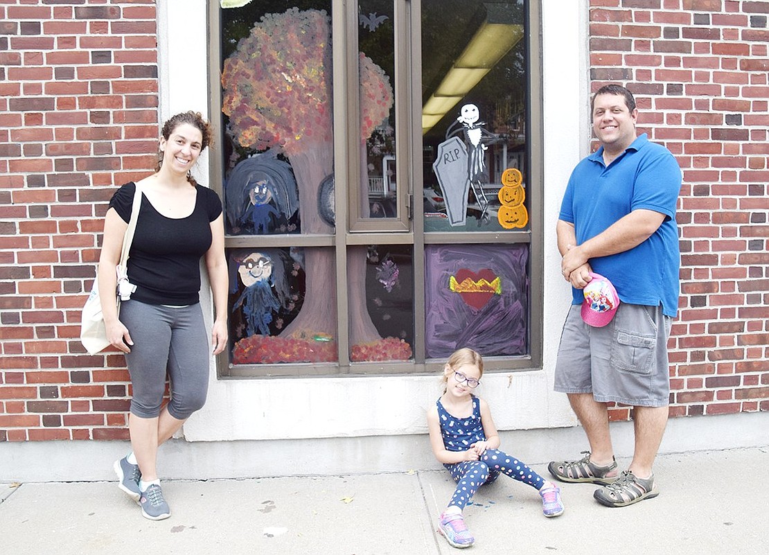 After covering a window with fall colors, nature, and characters from “The Nightmare Before Christmas,” the Butkiewicz family shows off their collaborative masterpiece. Locust Avenue residents Marissa and Russell brought their 6-year-old daughter Arianna to the library for some artistic bonding.