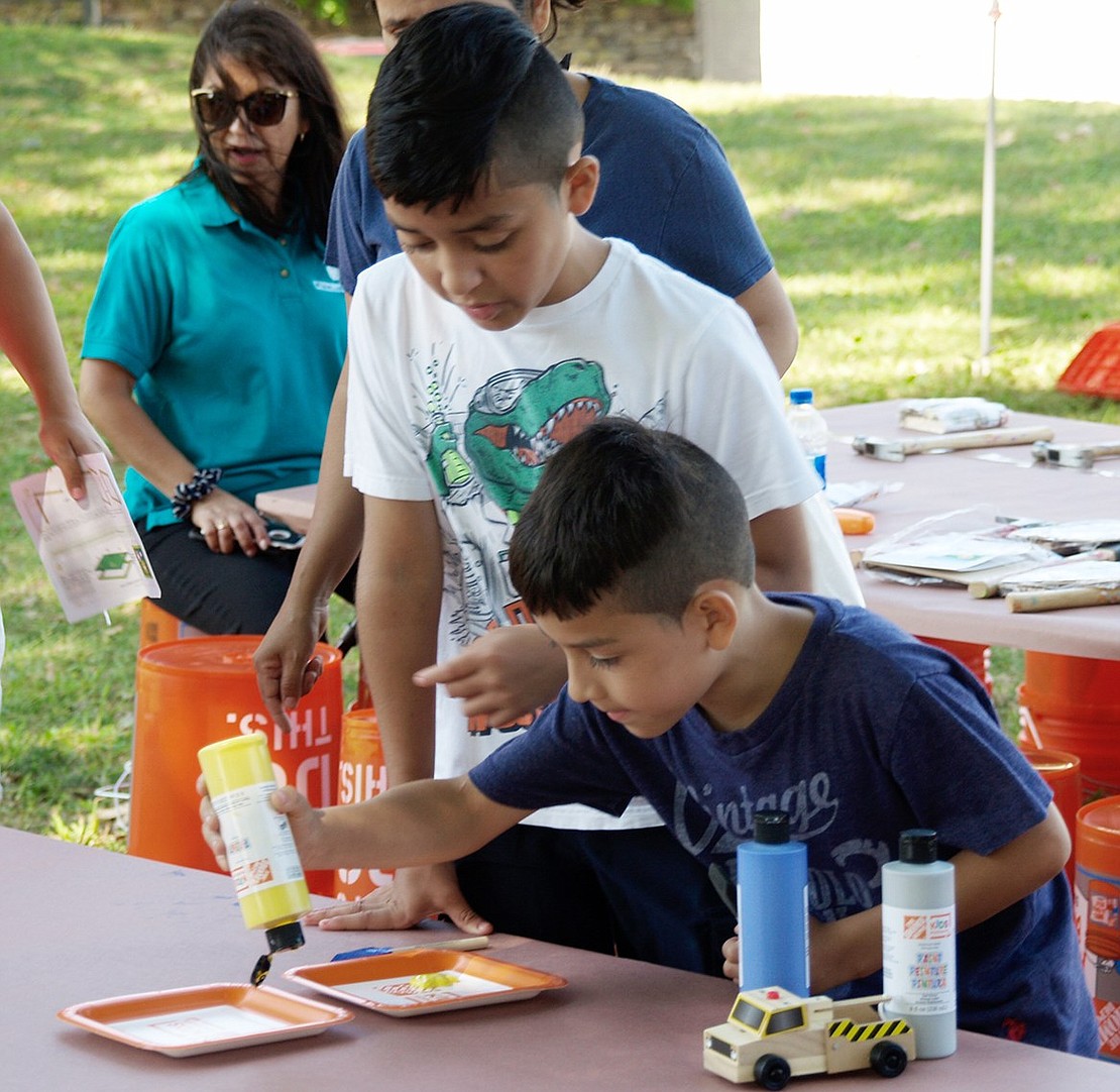 Grace Church Street resident Brandon Rodriguez, 10, stands over his 8-year-old brother James as he carefully squirts yellow paint onto a plate so they can decorate a wooden truck as part of a free workshop offered by The Home Depot. 
