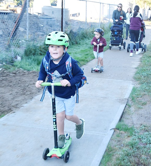 With a helmet matching his lime-green scooter, King Street School kindergartner Jack Hansbury zips to school faster than most walkers on Friday, Oct. 4. He’s followed by his brother Connor, 3, who joined the trip from their Alden Terrace home to celebrate International Walk to School Day, an annual event that encourages awareness of walking safety.