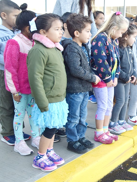 Bundled up in warm jackets, Charlotte Membreno (left), Gianlorenzo Ochoa and Sloane Shillingford, kindergartners in Alejandra Naselli’s class, stand on the curb and wait for the ceremony to begin.
