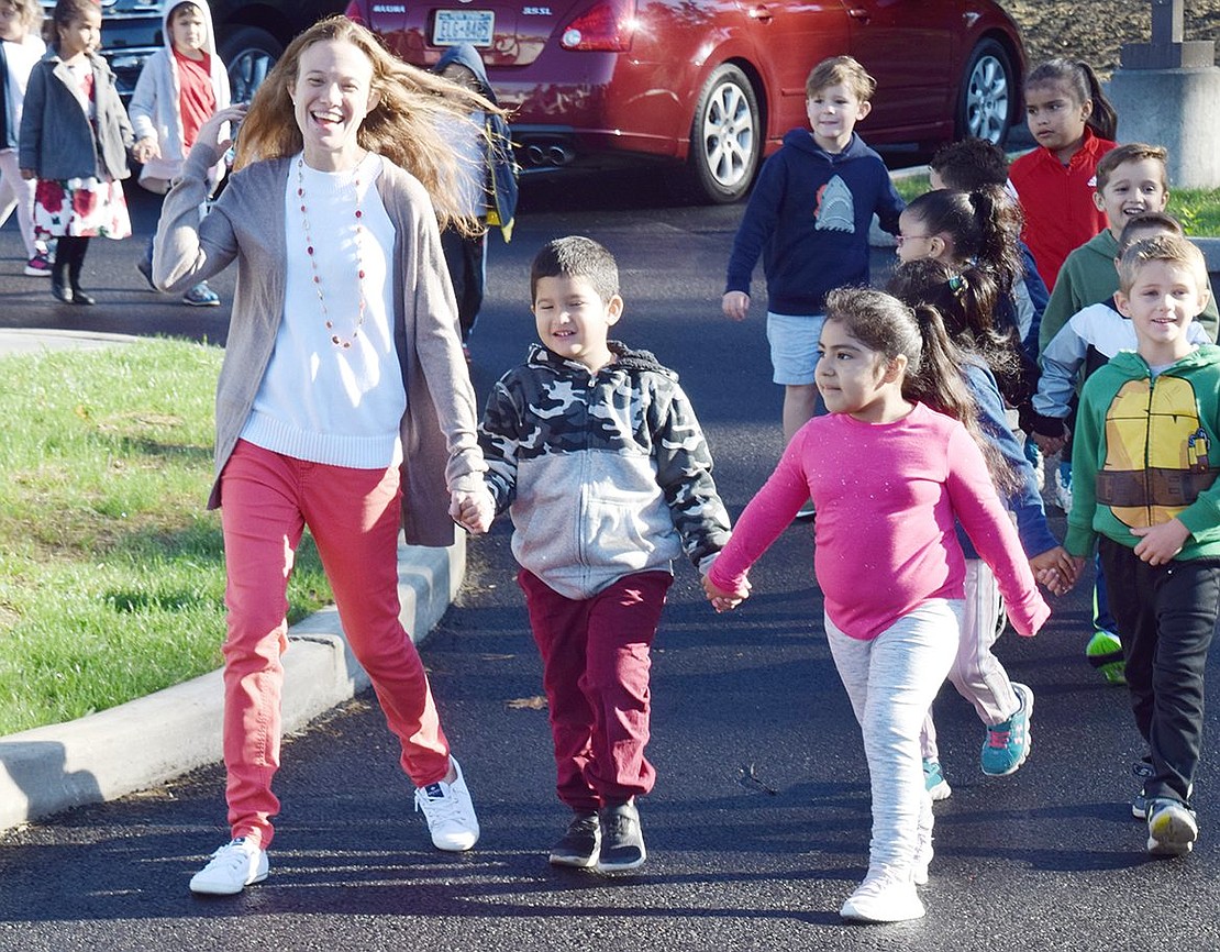 Kindergartners Sofia Mojica (right) and Julian Restrepo hold hands with their teacher Lindsay Renda as they stroll around the new parking lot. A communal walk following the ceremony is a Walk to School Day tradition.