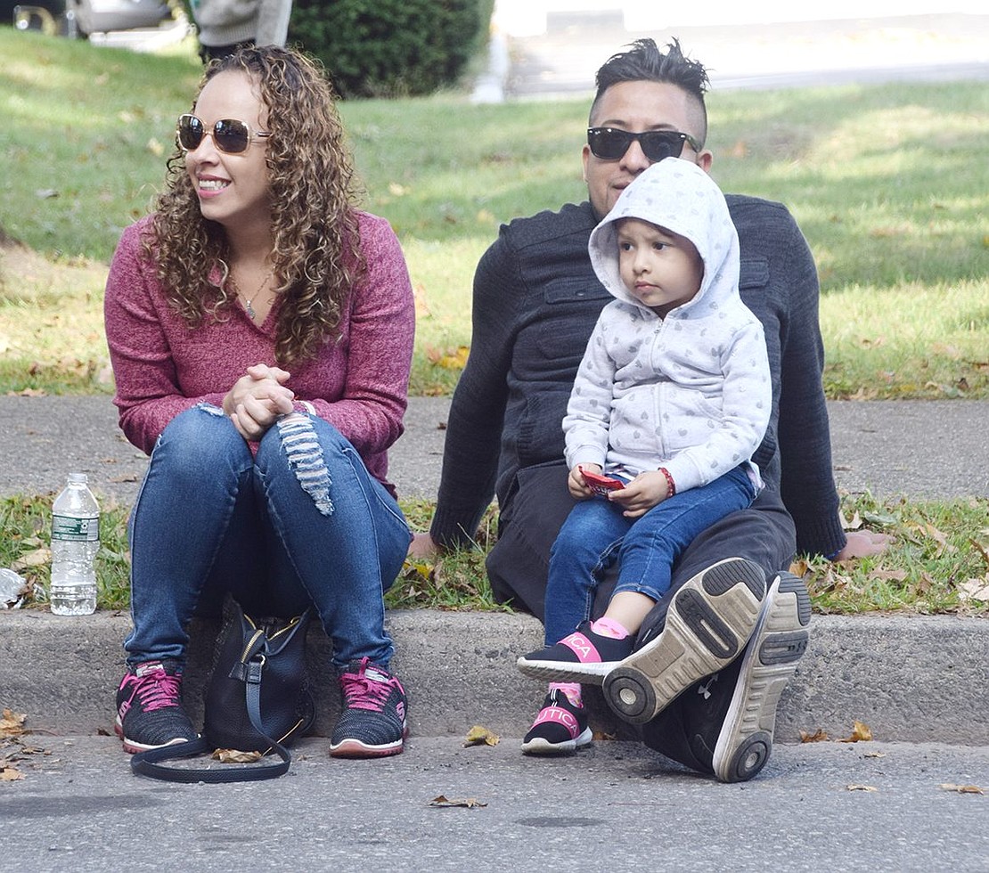 Sitting outside of the Ortiz Funeral Home on Westchester Avenue, Seymour Road residents Blanca Islas and Cayetano Aparicio grin as they watch the parade with their 3-year-old daughter Ahitana Samantha.