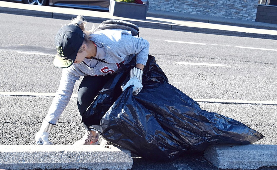 Downtown resident Jen Williams stops on her walk down Westchester Avenue to pick up trash with her gloved hands.