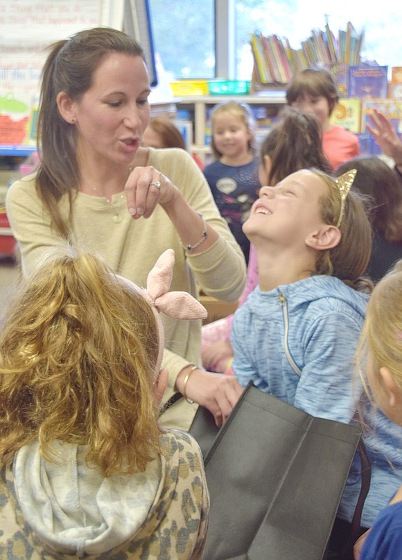 With eyes closed shut, first-grader Adriana Wright reaches into a bag and tries to correctly guess what item she is touching. Parent volunteers including Stephanie Sandarciero (left) filled the bags with items such as a sock, pencil and tinfoil.