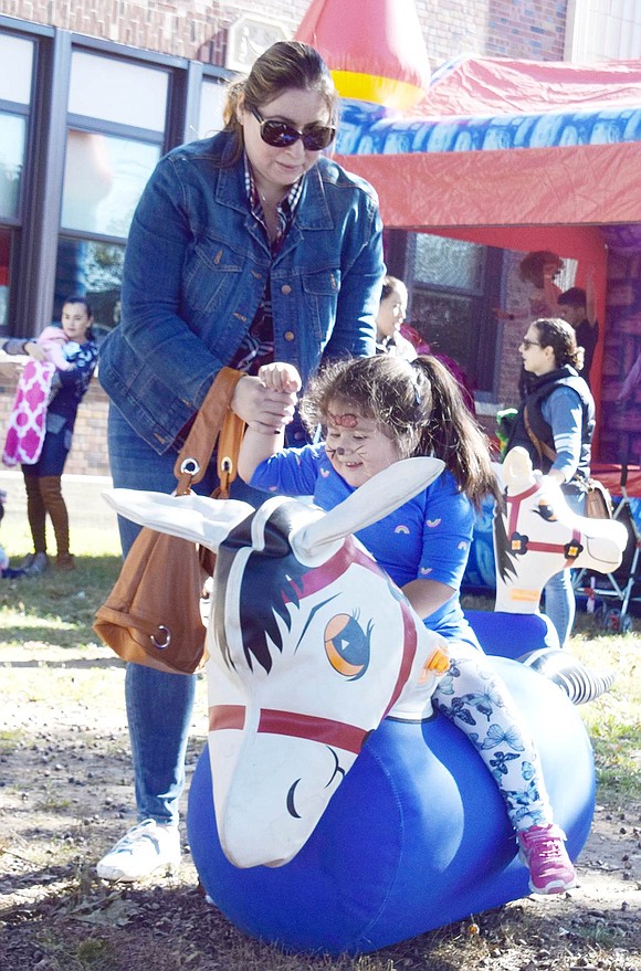 Natalia Bustelo, 3, holds onto her mother Carmen Novillo, Greenwich, Conn. residents, as she finds her balance on the inflatable bouncy horse at the Harvest on Park carnival.