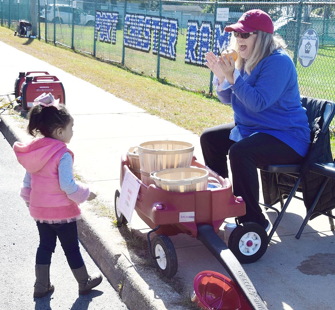 After throwing many tiny pumpkins at the baskets, 3-year-old Genesis Barrera is cheered on by Jean Lane, Rye Brook, resident and volunteer Leah Borzoni after she got a few in.