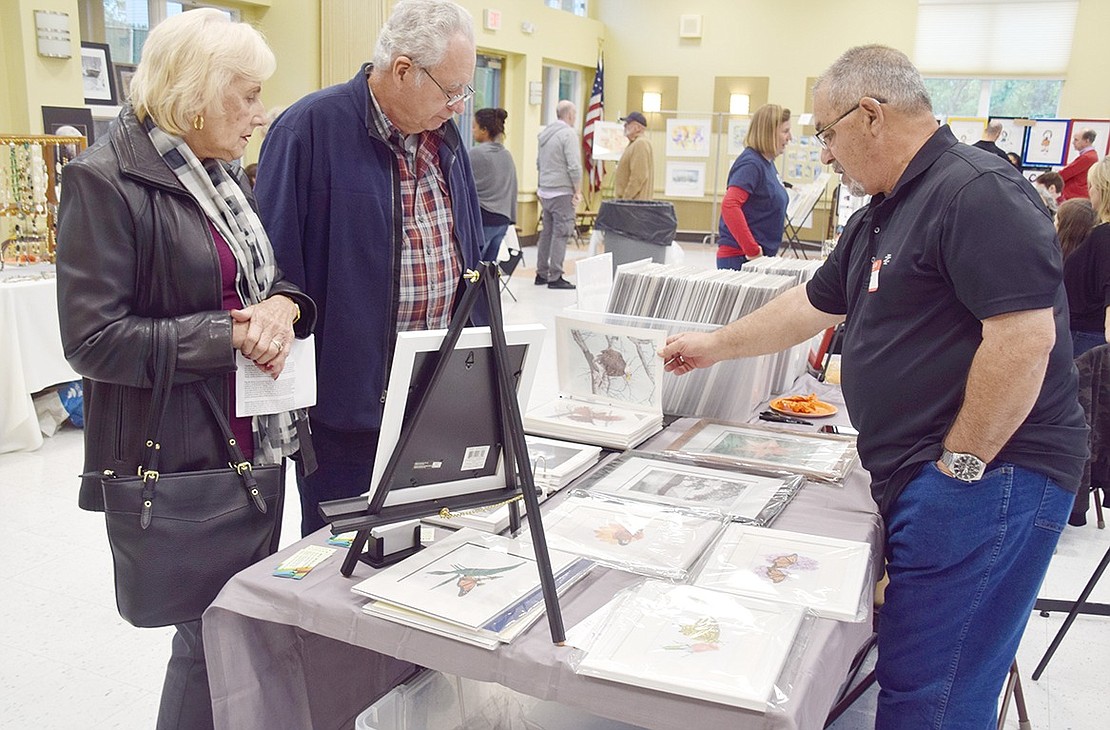 While perusing the different tables, Westchester Avenue resident Patricia Barr and her friend visiting from Cortlandt Manor Bob Westfall chat with Steve Rossi about his colored pencil bird sketches. Rossi, a Yonkers resident, is a Port Chester native.