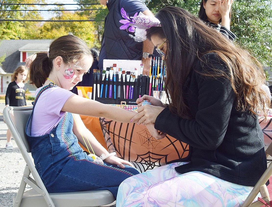 Ridge Street School third-grader Louisa Amestoy, 8, looks on as glitter dolphins are painted on her forearm. Keeping with the theme of Halloween, hairstylists and glitter tattoo artists like Perla Chen of Silly Cheeks face painting company (right) were hired for the festival to help children get dressed up.