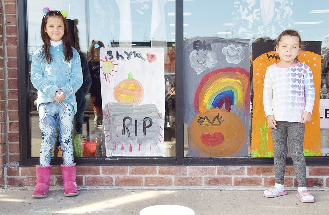 Ridge Street School first-graders Shyla Schroeder (left) and Ella Pohlman stand in front of their spooky works of art at Rye Ridge Shopping Center.