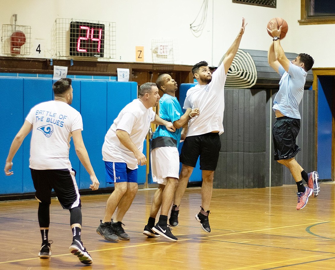 Phys ed teacher Jonathan Plato jumps up to shoot a basket which Police Officer Andy Polanco tries to block.