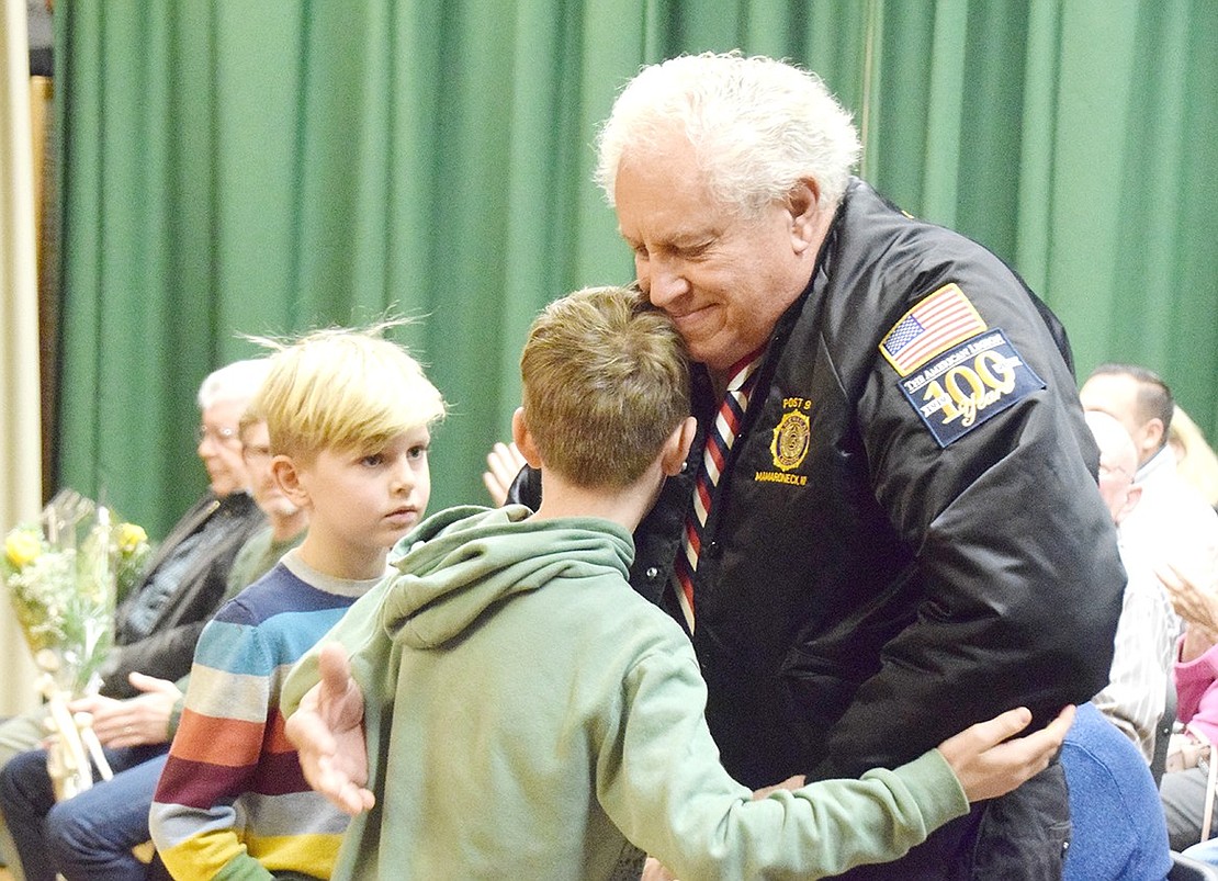 U.S. Navy veteran Kenneth Sunderland kindly embraces his neighbor Wessel Aarts, a King Street School third grader, on stage in the elementary school’s auditorium. Aarts and his second-grade brother Jacco (left) presented Sunderland with a rose during the school’s annual Veterans Day Ceremony on Friday, Nov. 8.