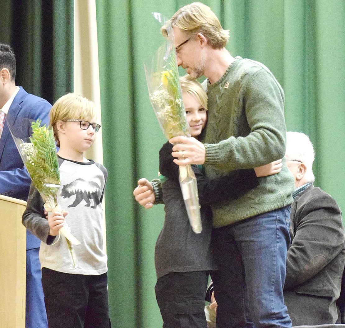 King Street School fourth-grader Jonah Helmle gives his father Carl a hug during the rose giving ceremony at the end of the celebration. Carl’s other son Evan, a second grader, patiently waits for his turn.