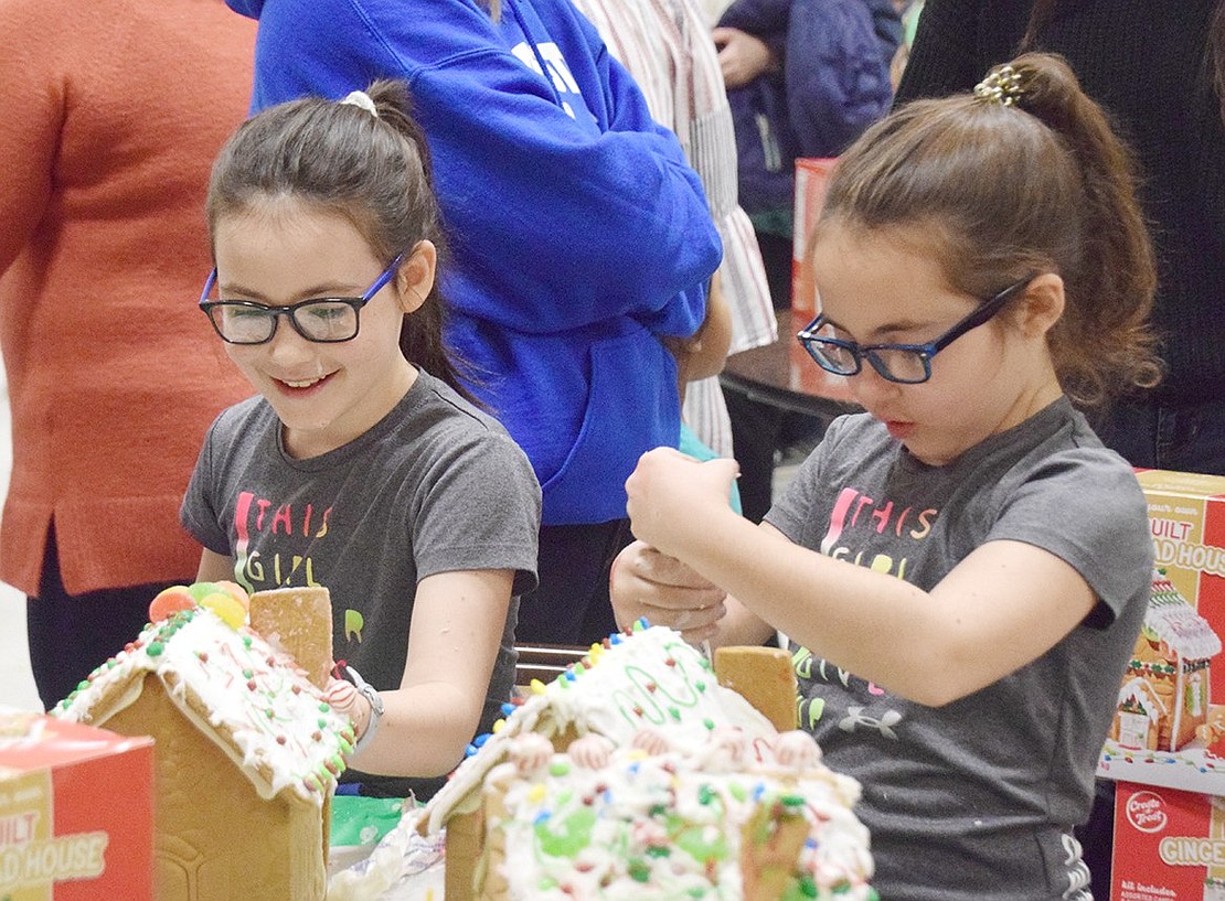 Park Avenue Elementary School fourth-graders Jamie (right) and Ryann Onofrio-Franceschini smile as they apply frosting and other decorations to their gingerbread houses. The Port Chester residents are two of the 45 participants attending the first Gingerbread House Craft Night on Friday, Nov. 22 at the Anthony J. Posillipo Community Center on Garibaldi Place. It was sponsored by the Rye Brook Recreation Department.