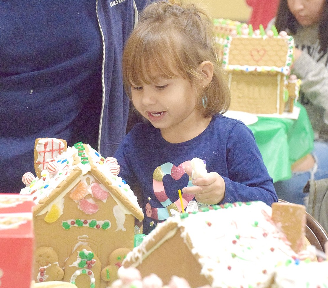 With a frosting tube in hand, Whittemore Place resident Jenny Morano, 3, happily tries to apply the sweet treat to her gingerbread house rather than her face.