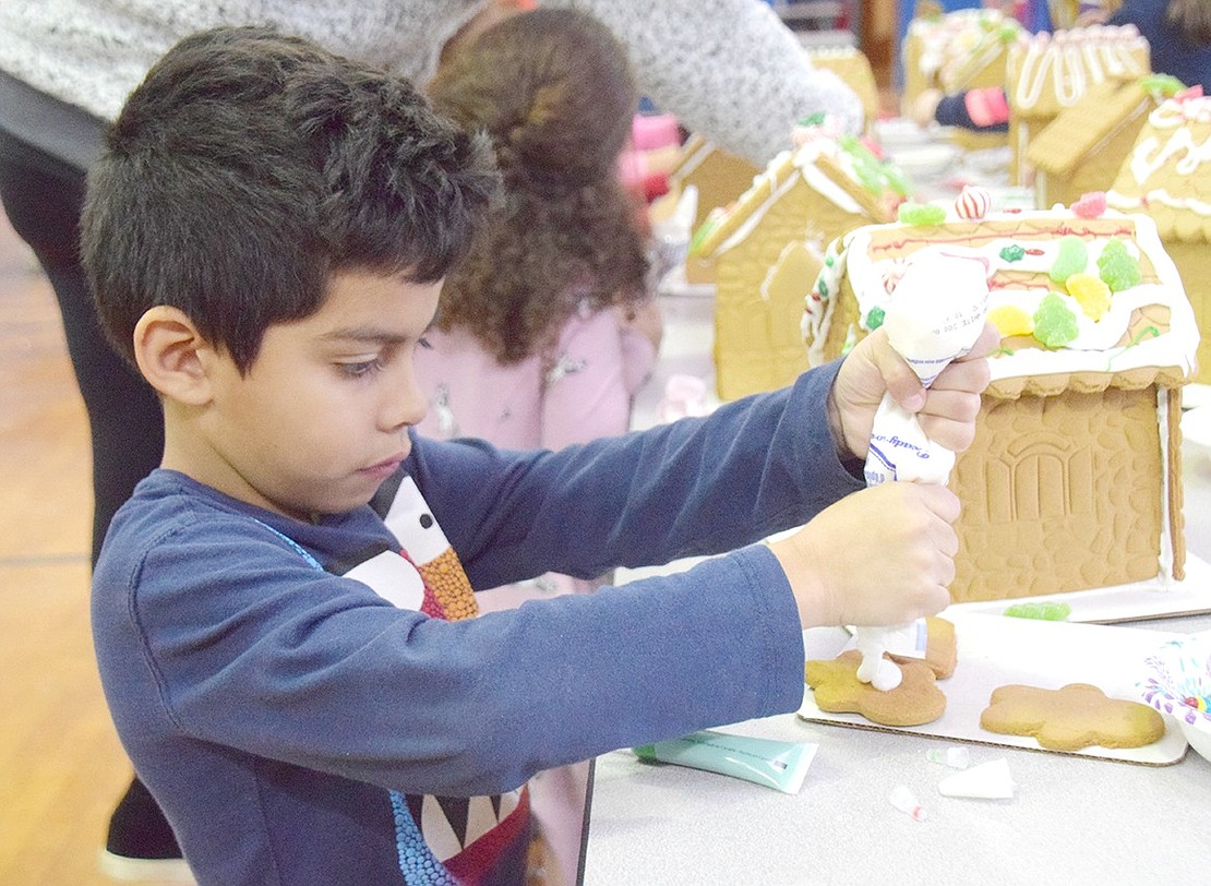 Using frosting as a glue, first-grader David Lima sharply focuses on application so he can stick a gingerbread man onto his colorful cookie home.