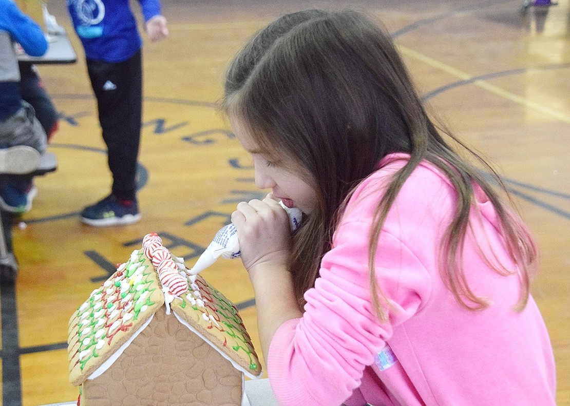 First-grader Savannah Gimenez uses both hands to delicately squeeze frosting from a tube into decorative dots on the roof of her creation.