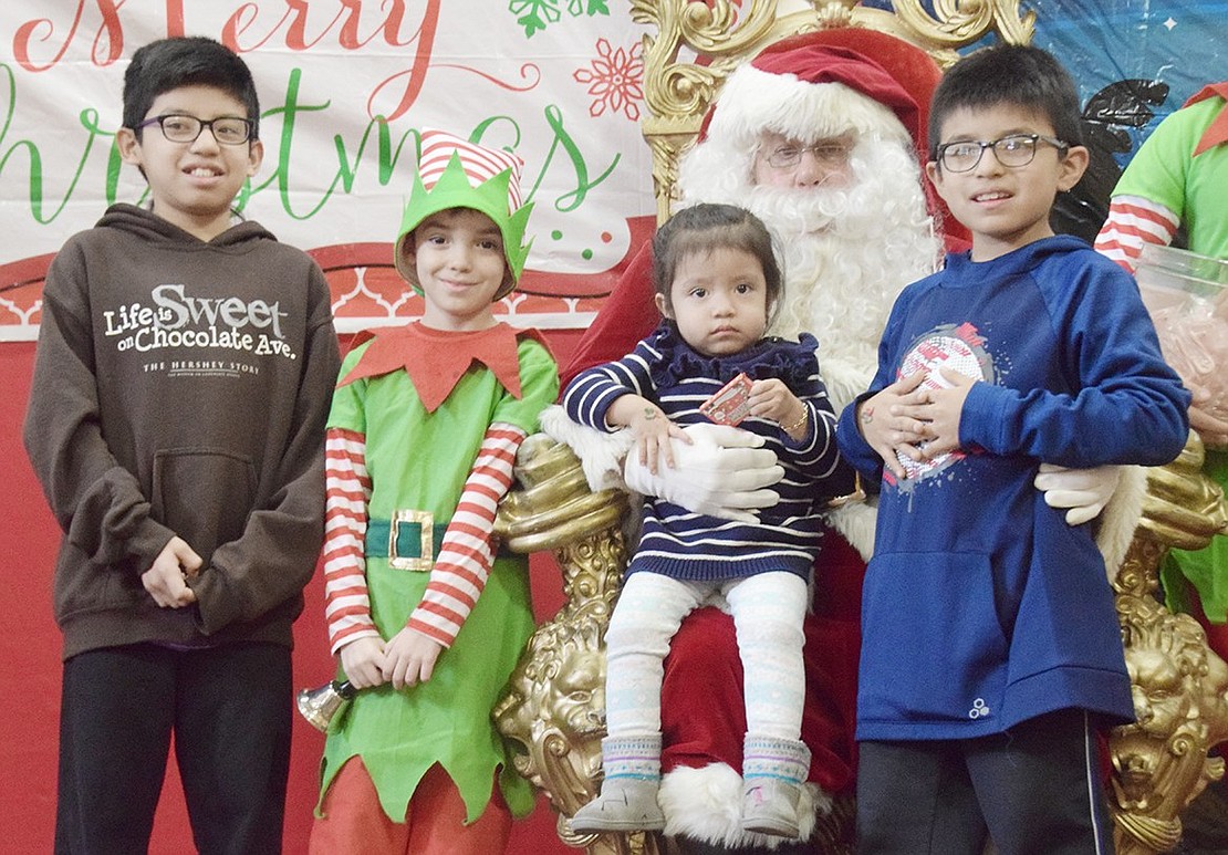 Siblings and Willett Avenue residents Jacob Gordillo (left), 11, Amy, 3, and Michael, 9, pose for a photo with Santa Claus and his elf, played by 8-year-old Logan Massa.