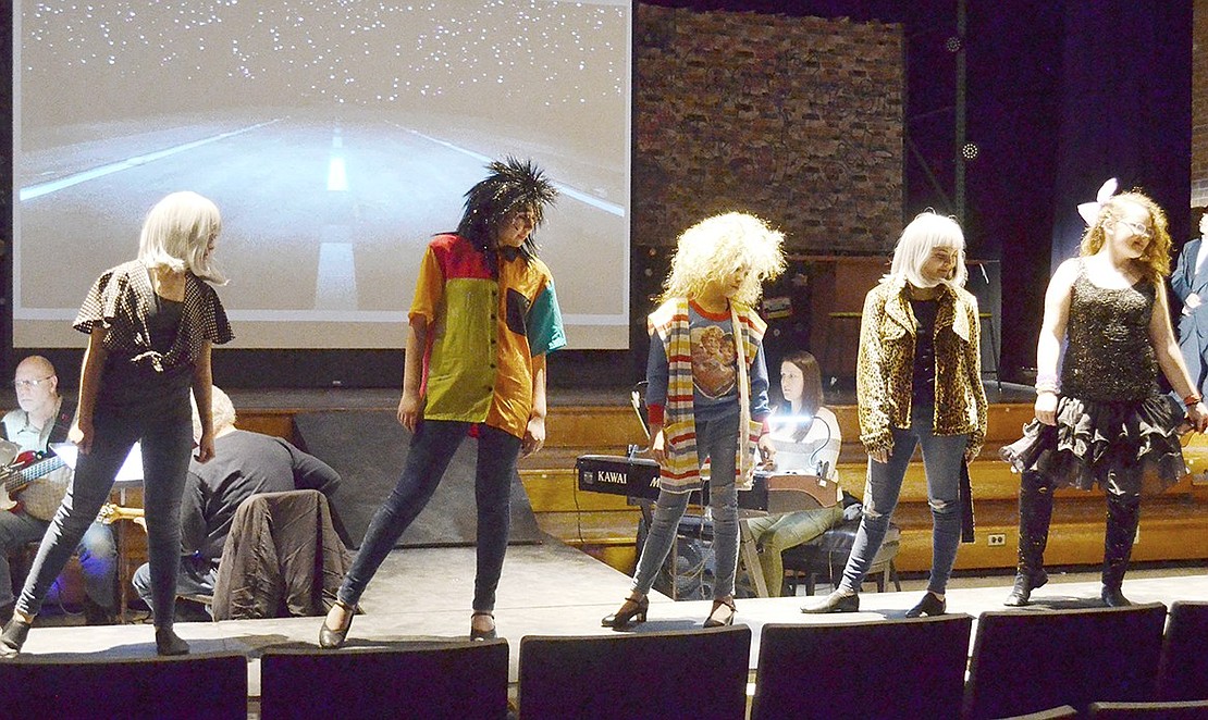 With crazy hair and funky outfits, female ensemble members perform a slow, captivating routine while men lining the sides of the stage sing a rendition of “Waiting for a Girl Like You,” originally by Foreigner.