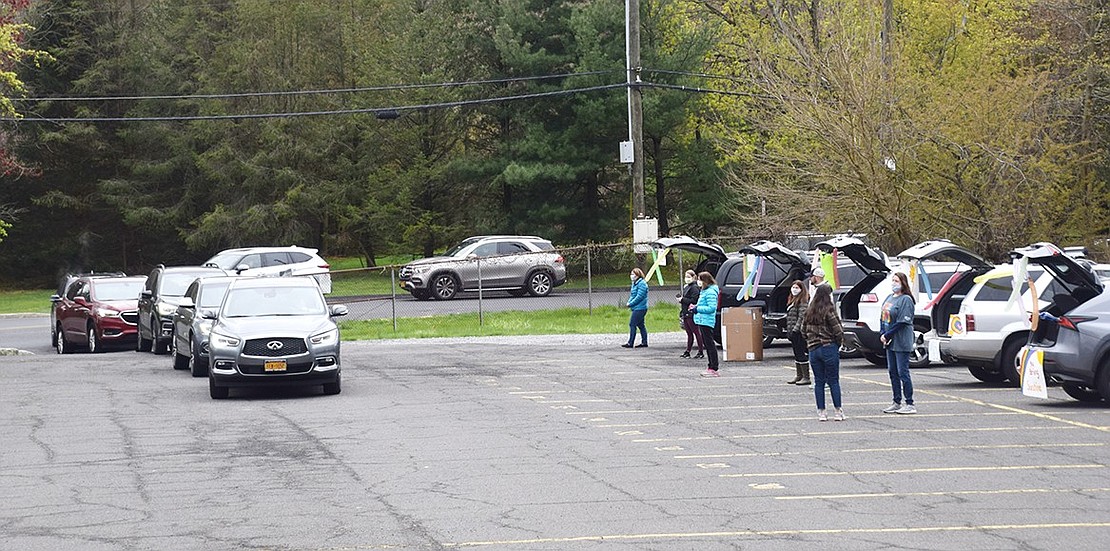 Teachers wait near their decorated cars as their students drive by and wave.