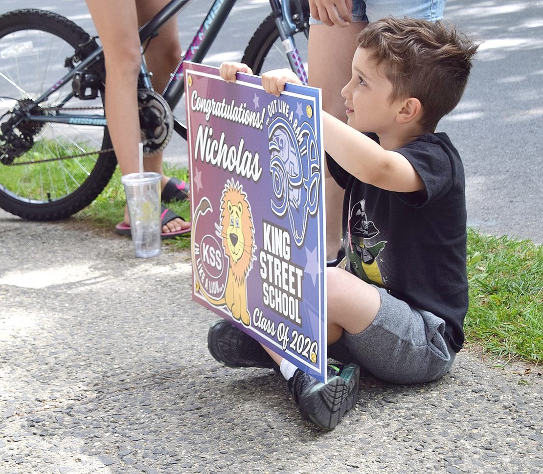 Helping to support his older schoolmates, kindergartener Luke Petriella sits and waits patiently to give the adults a sign for Nicholas to hang. The posters were designed by PTA co-president Jill Geller and printed by Vinnie Pinstripe.