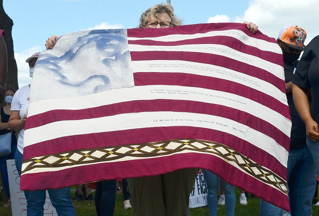 Larchmont resident Ruth Obernbreit Glass unveils a flag with the words of Bartlet Shanklyn, who escaped slavery, inscribed on it. The textile was made by artist Tina Maria Dunkley.