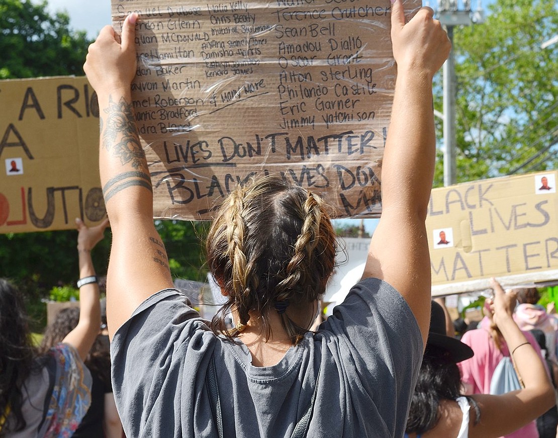 White Plains resident Carina Sasso holds up a sign listing some of the names of those who have been killed by police brutality.