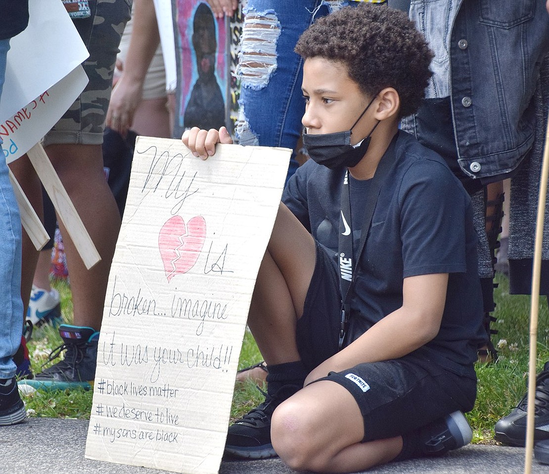 With a sign speaking to broken hearts, Port Chester elementary school student Sir Anthony Foust kneels and listens to orators at the protest as he prepares to make his own speech about abolishing racism and loving each other as a community.