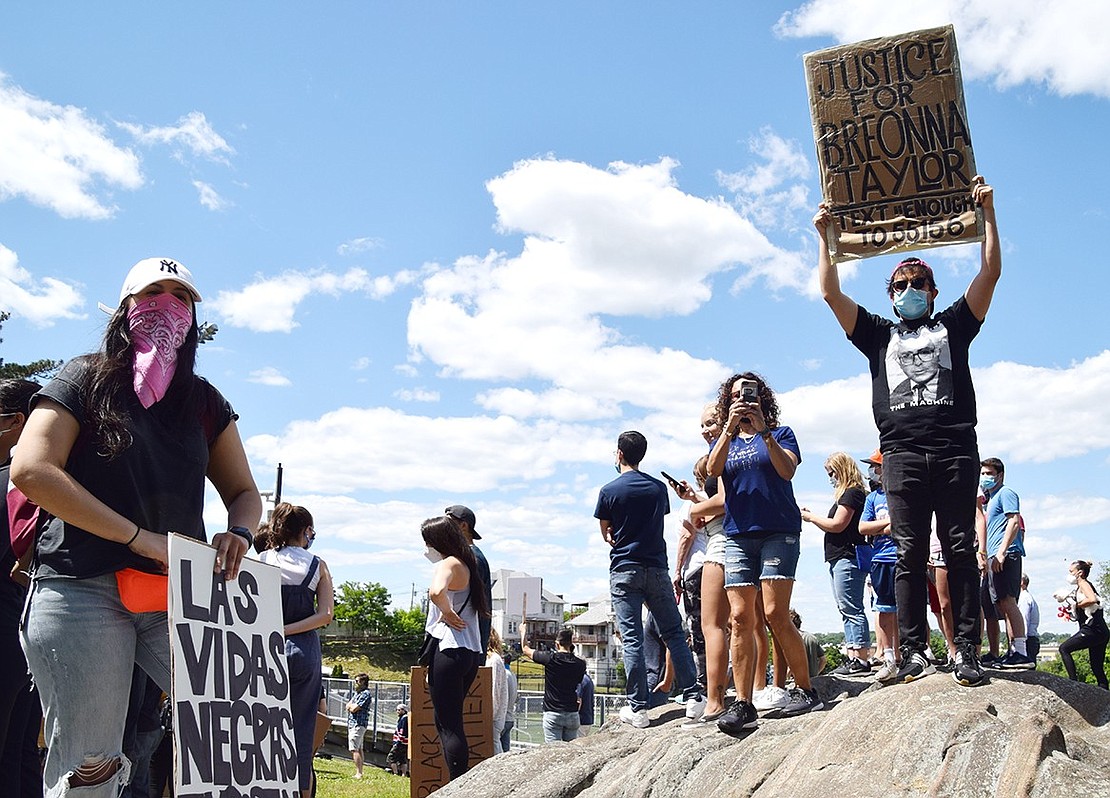 Standing tall on top of a rock at Columbus Park, a man waves a poster to passing marchers reading “Justice for Breonna Taylor.”