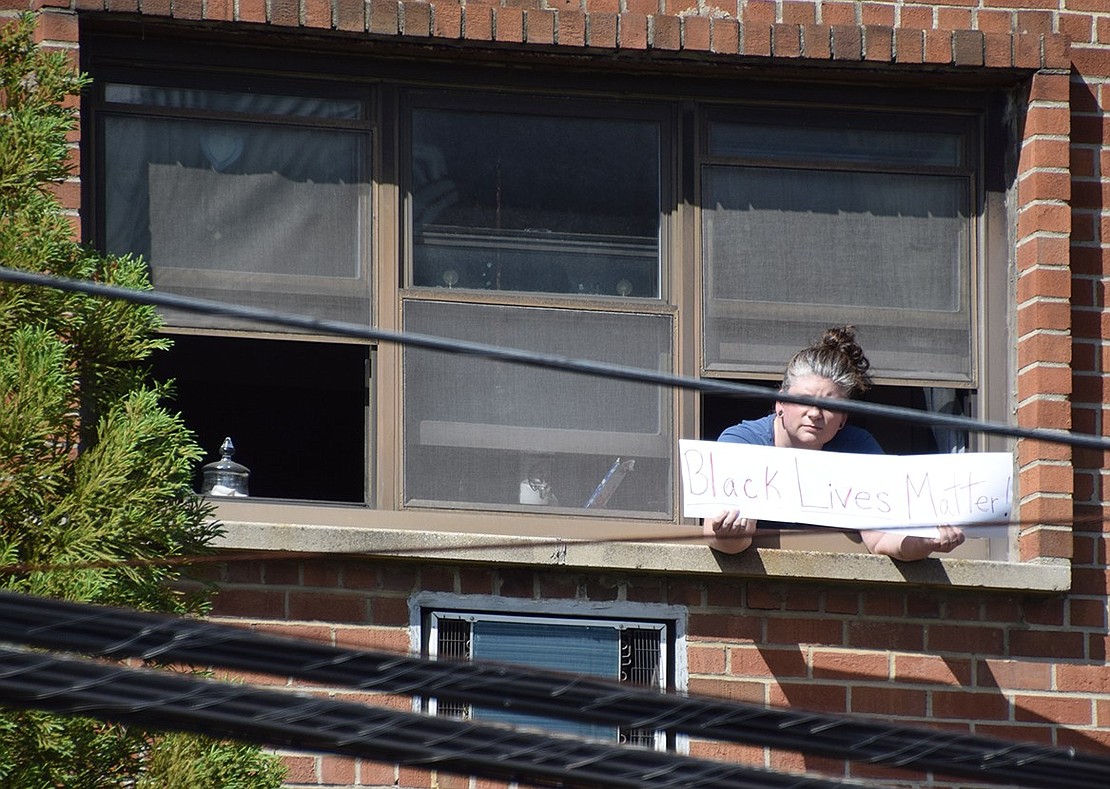 Showing support from afar, a woman hangs out the window of her apartment at the corner of Westchester Avenue and Regent Street as the procession pauses for more speeches and chants.