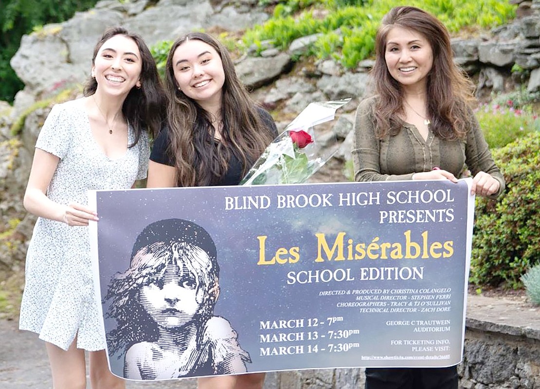 Dance captain Sophia Mullaly (middle) smiles with her sister Julia, a Blind Brook High School theater alumna, and her mother Kazumi as they hold up a “Les Misérables” banner.