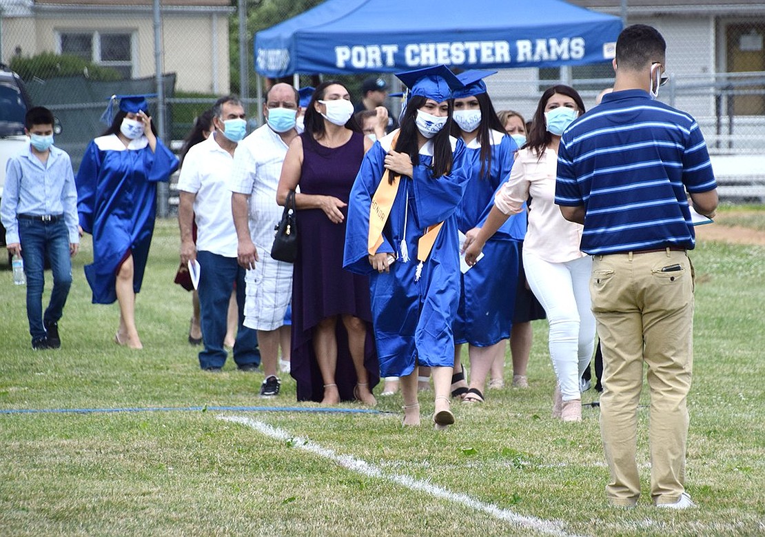 As graduates and their families approach Jeffrey Kravitz to the tune of “Pomp and Circumstance,” the history teacher guides them to their assigned socially distanced box.