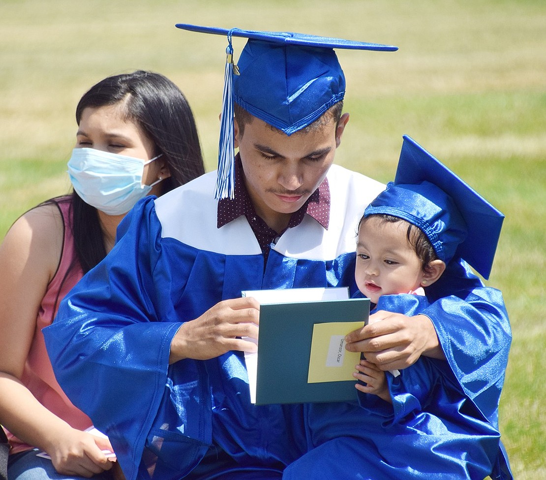 After retrieving his diploma and returning to his designated box, Oscar Umanzor opens the booklet to check it out with the help of his daughter Kelsey, who wears a matching blue cap and gown.