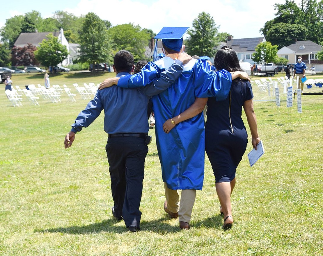 As “Pomp and Circumstance” echoes across the field, Joseph Tapia Guzman walks arm in arm with his mother Delia Guzman and father José Tapia as they approach the graduation ceremony.