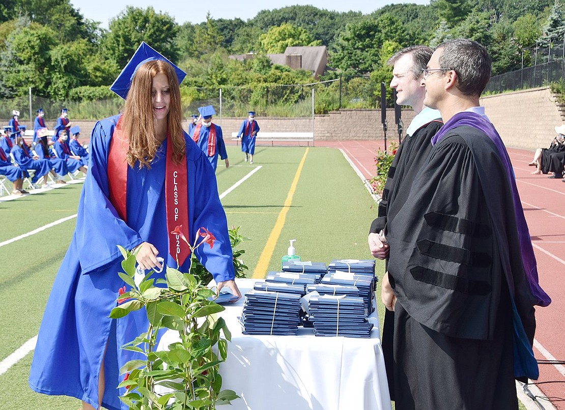 After gracefully walking across the field, Sarah Cassuto picks up her diploma from a table manned by Board of Education President Ryan Goldstein (front) and former High School Principal Derek Schuelein.