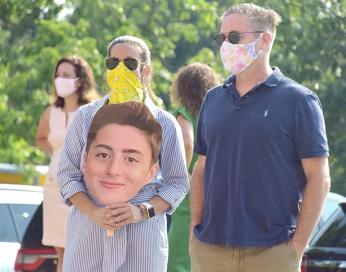 As graduates walk into the commencement ceremony, Jenn and David Steinthal cheer them on in the parking lot while holding a large photo cutout of their son, Wyatt.