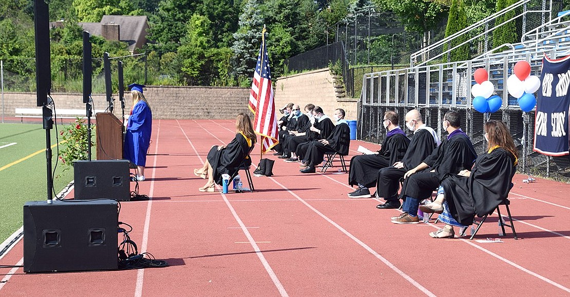 Blind Brook administrators sit in a socially distanced line behind the podium for an unusual outdoor graduation ceremony.