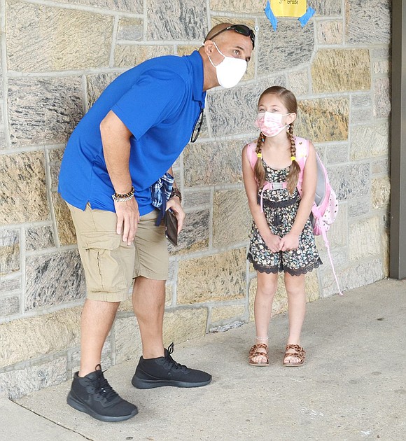 While wearing a fashionable pink face mask, third-grader Carly Dutra tells her father Sean all about her first day back at school.