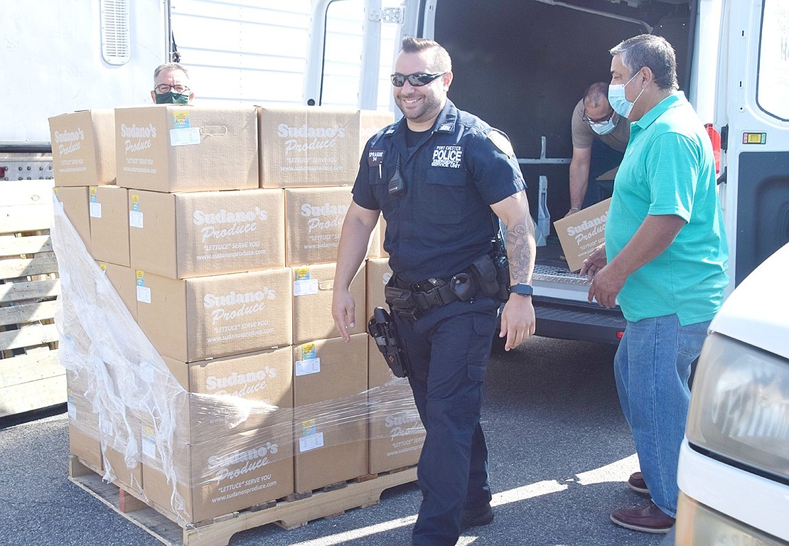 Port Chester Police Officer Michael Sprague smiles as he and others fill a Neighbor to Neighbor truck with boxes stuffed with produce, a gallon of milk, eggs and a chicken amongst other edible items.