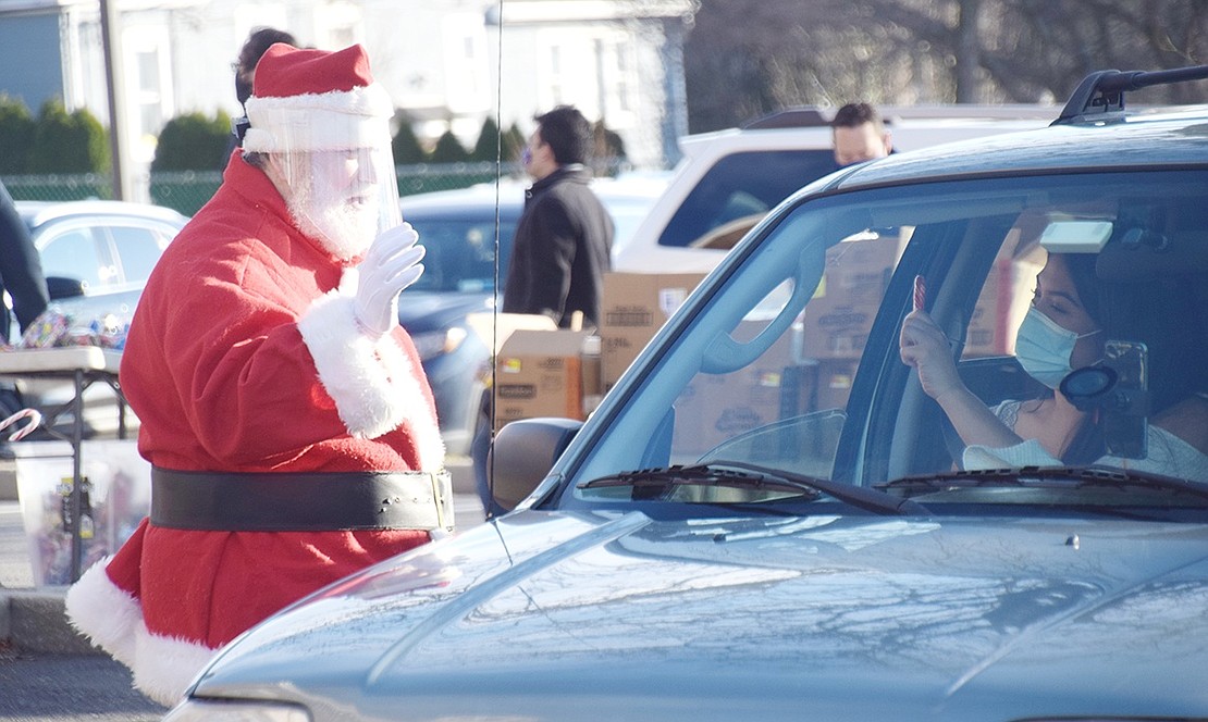 To stay safe during the COVID-19 pandemic, Santa Claus waves from a distance with a face shield on.