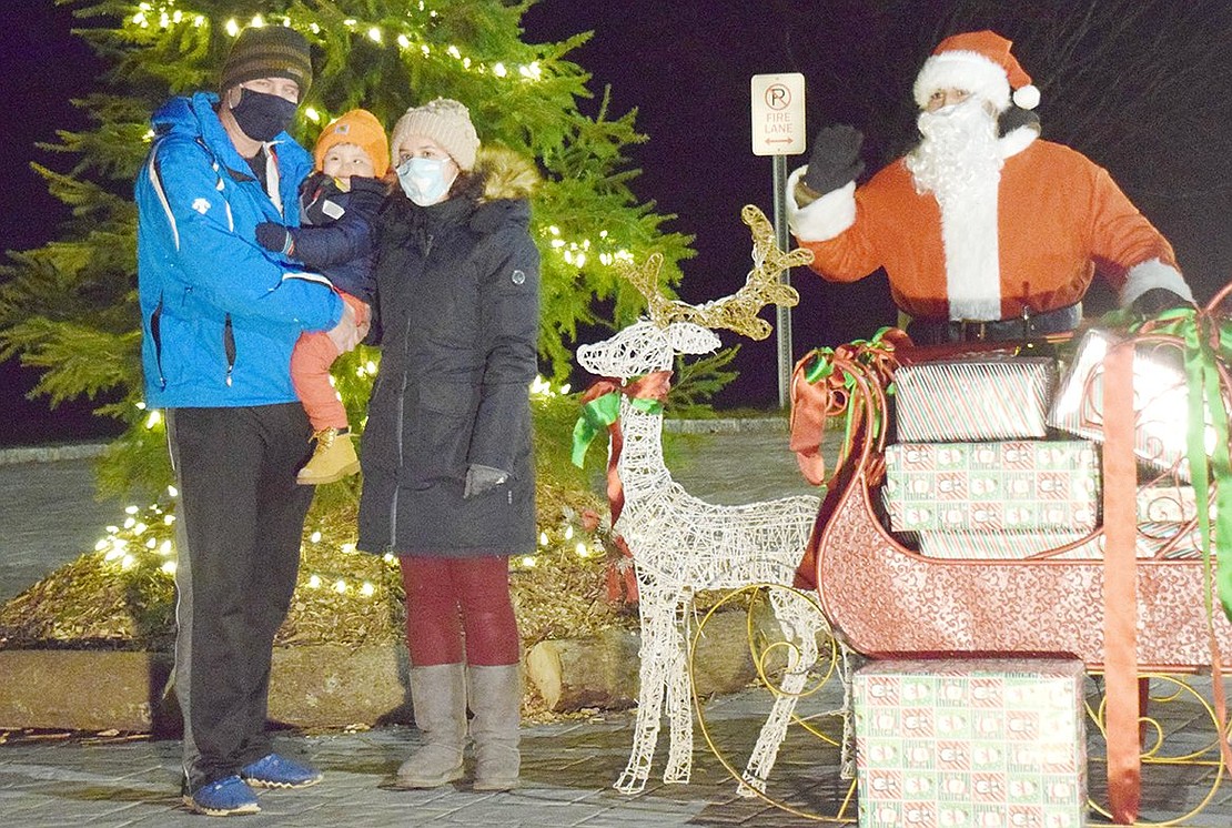 Happy as can be, Breckenridge Avenue resident Jayden Valente, 2, snuggles between his parents Marco and Danielle as they pose for a photo six feet away from Santa (played by Andrew Marroquin). After a long night of delivering gifts around the world, Mr. Claus made one last stop at Crawford Park on Saturday, Dec. 26, to spread cheer to the community at the Rye Town-sponsored Holiday Drive Through Celebration.