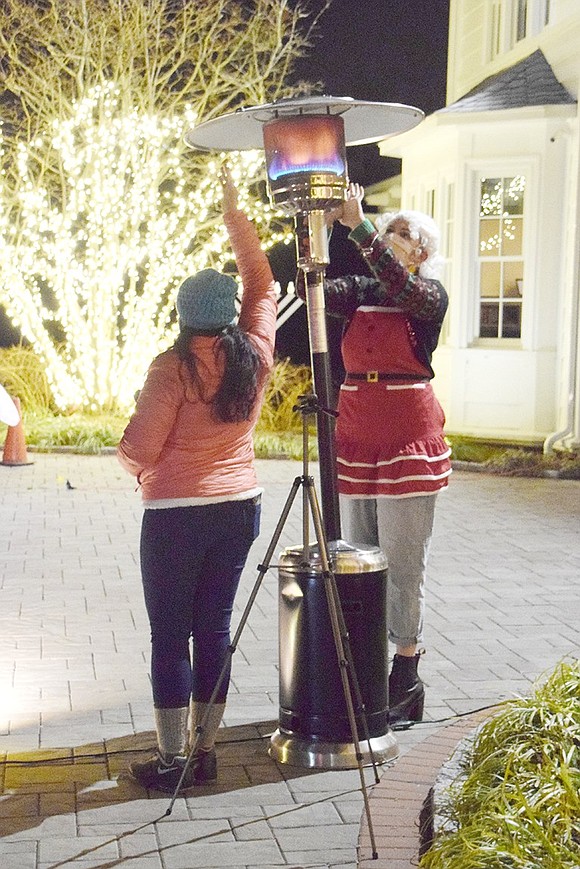 Between families approaching for a Christmas photo, Mrs. Claus (played by Blind Brook High School senior Kate Jaffee) and photographer Naomi Bowen warm their hands up by the patio heater.