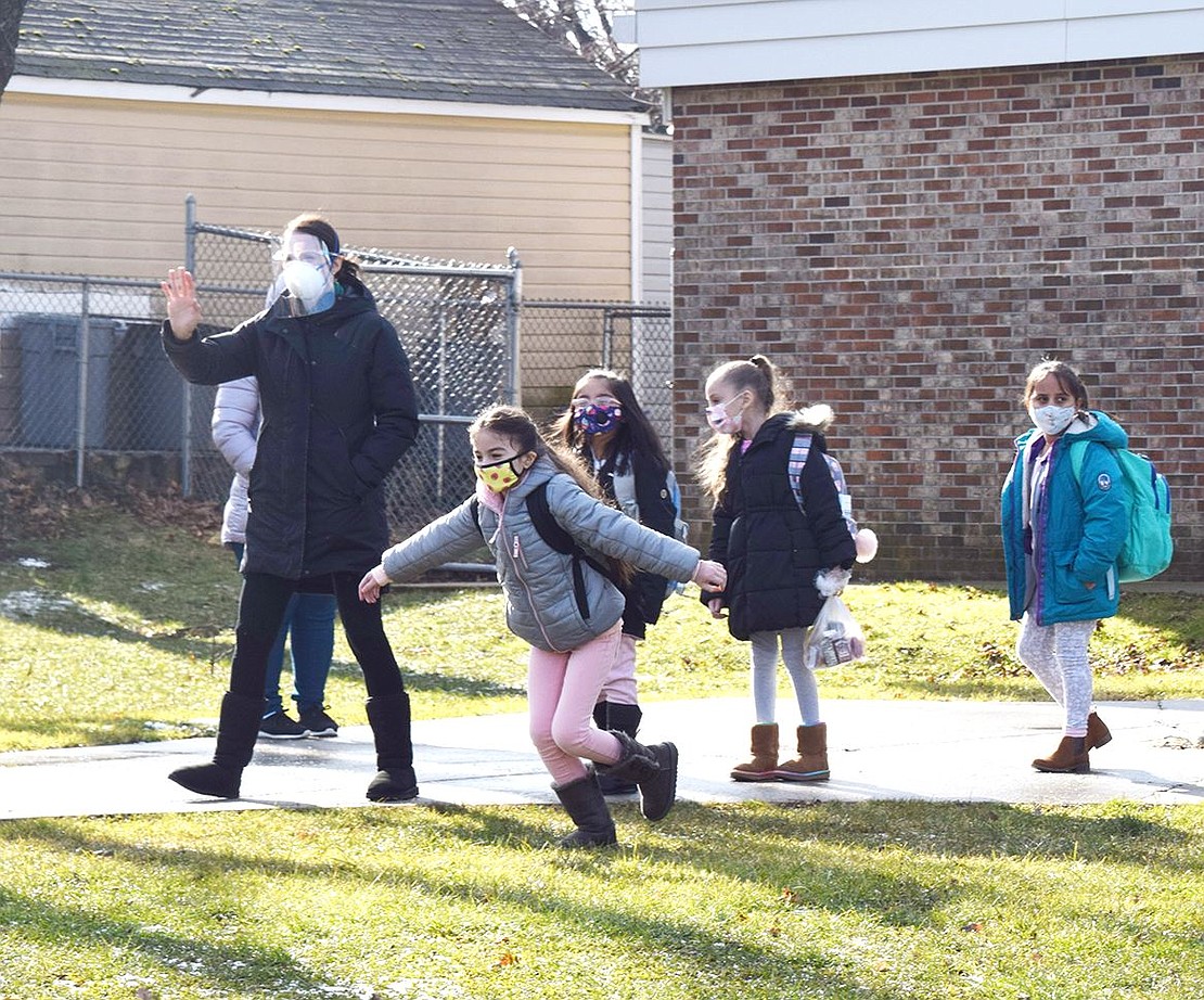 Protected by a face shield and mask, John F. Kennedy Elementary School second-grade teacher Cristina Alampi waves at parents as she leads her morning class of students out of the building for pickup.